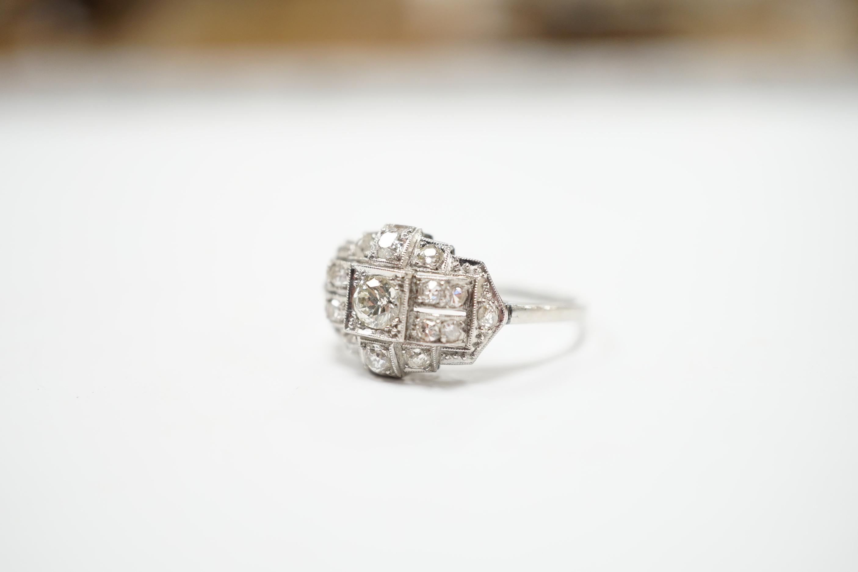An Art Deco style white metal and millegrain set diamond cluster ring, size N/O, gross weight 4.1 grams, the central stone with a diameter of approximately 4.5mm.